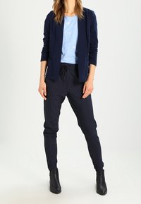 Granatowa marynarka na jasnoniebieskim t-shircie, zestawiona z granatowymi dresami w paski. Czarne botki do kostki dopełniają strój. Gładkie i dopasowane kroje.