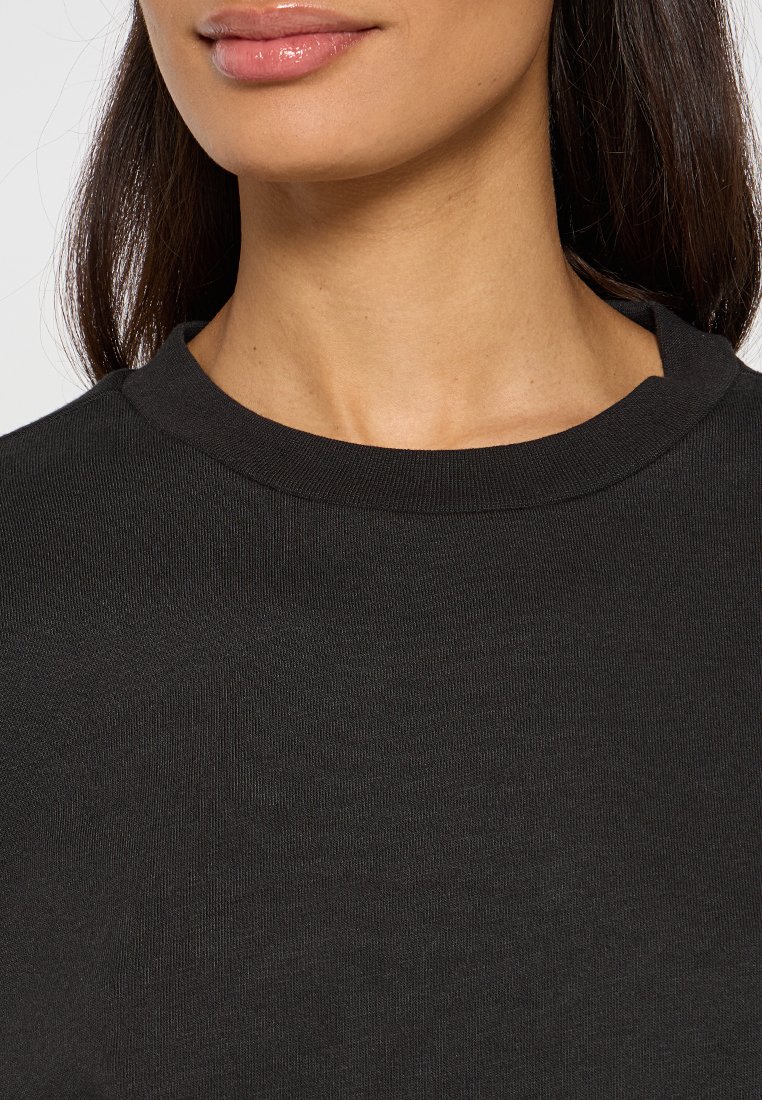 Camiseta negra de cuello redondo con una tela suave y texturizada. La vista en primer plano muestra el detalle de costura alrededor del escote.