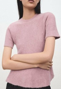 Pull à manches courtes, rose clair, en maille douce, avec un col rond et un ourlet inférieur légèrement évasé.