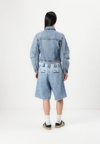 Conjunto de chaqueta de mezclilla y pantalones cortos en azul claro, con un diseño corto, costuras clásicas y dos bolsillos traseros. Combinado con zapatillas negras y calcetines blancos.