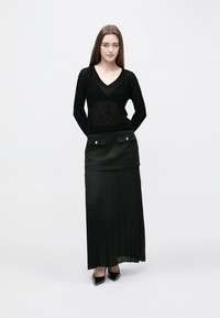 Črna majica z dolgimi rokavi in V-izrezom z nežnim sijajem; kombinirana s črno, nabrano maxi krilo z žepi spredaj in okrasnimi gumbi.
