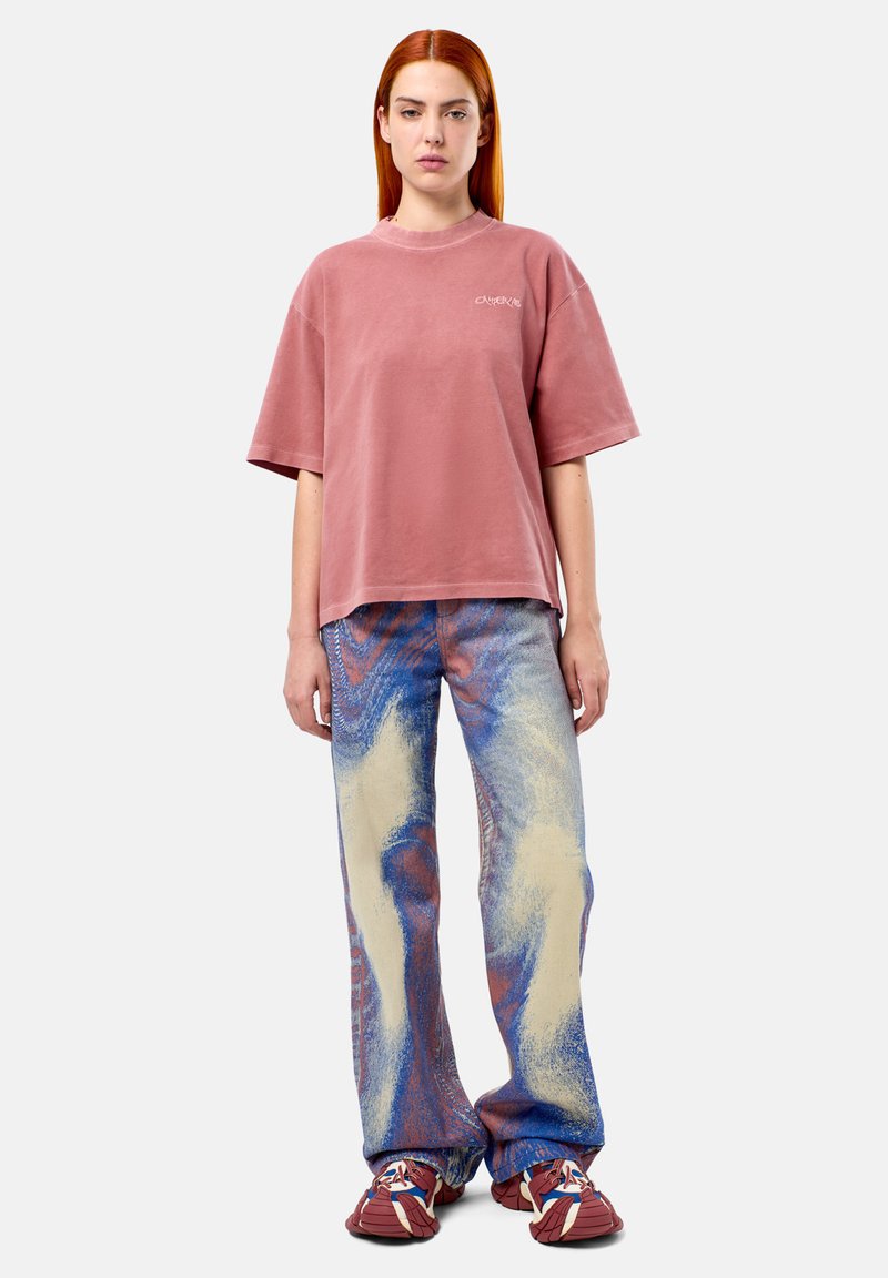 Oversized dusty pink cotton t-shirt paired with abstract patterned blue and cream wide-leg pants and brown sneakers.