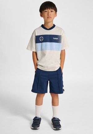 Biała koszulka z niebieskimi poziomymi paskami i logo, w połączeniu z granatowymi szortami. Koszulka ma krótkie rękawy oraz kontrastujący kołnierzyk.
