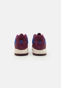 Bakgrunnsvisning av sportssko med en maroon overdel og blå detaljer, polstret såle og teksturert hældetalj.