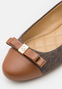 Chaussure plate avec bout en cuir marron, dessus en tissu à motif, semelle intérieure beige matelassée et nœud décoratif avec détail logo doré.