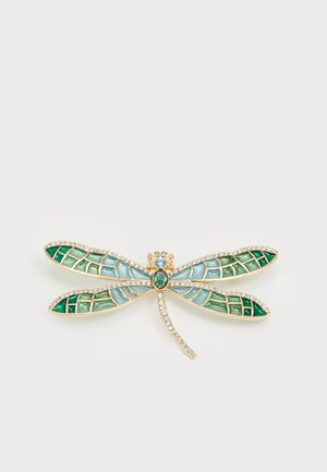 Brož ve tvaru vážky ze žlutého kovu. Má modré a zelené skleněné křídla se geometrickými vzory a krystalový akcent na těle.