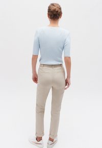 Lichtblauw geribbeld topje met korte mouwen gecombineerd met beige strakke broek, met een opgerolde zoom, gezien vanuit de achterkant, met witte sneakers.