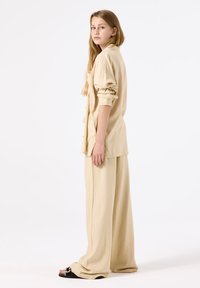 Beige, loose-fitting shirt and wide-leg pants, both made of lightweight fabric. The shirt has rolled sleeves and a chest pocket.