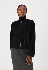 Black zip-up jacket with a textured, fluffy material and a high collar, paired with a ribbed gray skirt.