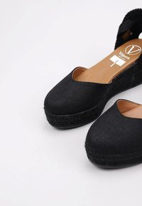 Sandalias de cuña de esparto negras de lona con punta redondeada, detalles de cuerda de yute y diseño de talón abierto. Forro interior suave visible.