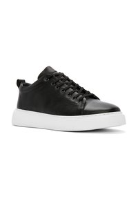 Sneaker in pelle nera con design a lacci, punta rotonda, suola in gomma bianca e un'etichetta sul retro. Texture liscia e stile minimalista.