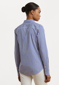 Blue and white striped long-sleeve shirt with a classic collar, buttoned cuffs, and a curved hem; cotton fabric with a smooth texture.