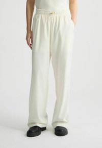Lichtcrème wijde broek met een elastische tailleband en een trekkoord. Gemaakt van soepel stof. Gepaard met zwarte schoenen. Minimalistisch ontwerp.