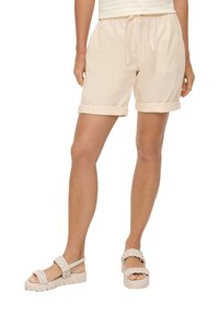 Beżowe szorty z elastycznym pasem i sznurkiem, z podwiniętymi nogawkami i luźnym krojem. W zestawie z lekkimi plecionymi sandałami na teksturowanej podeszwie.