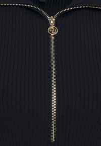 Maglione nero a coste con colletto alto, dotato di una cerniera dorata e dettagli hardware, che mette in risalto un tessuto texturizzato.