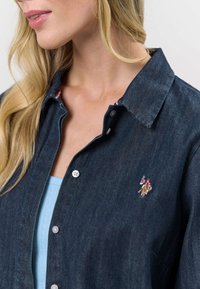 Donzen overhemd in donkerblauw, met een knoopsluiting, puntkraag en een klein geborduurd logo op de borst. Glad van textuur.