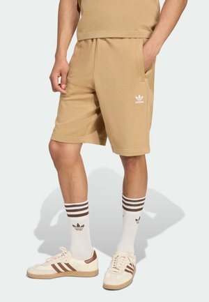 Tan cotton-blend shorts with elastic waistband, side pockets, and white logo. Paired with white and brown striped socks and beige sneakers.