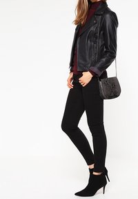 Černá kožená motocyklová bunda, vínový rolák, černé skinny džíny a černé kotníkové boty. Texturovaná černá taška s řetízkem.