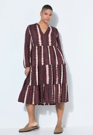 Kvinde iført en langærmet, V-hals, burgunder- og hvidstribet lagdelt midikjole med beige slip-on sko mod en hvid baggrund.