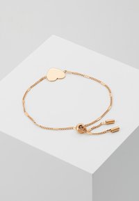 Gold-colored bracelet featuring a heart-shaped charm, a chain with adjustable length, and decorative metal accents at each end.