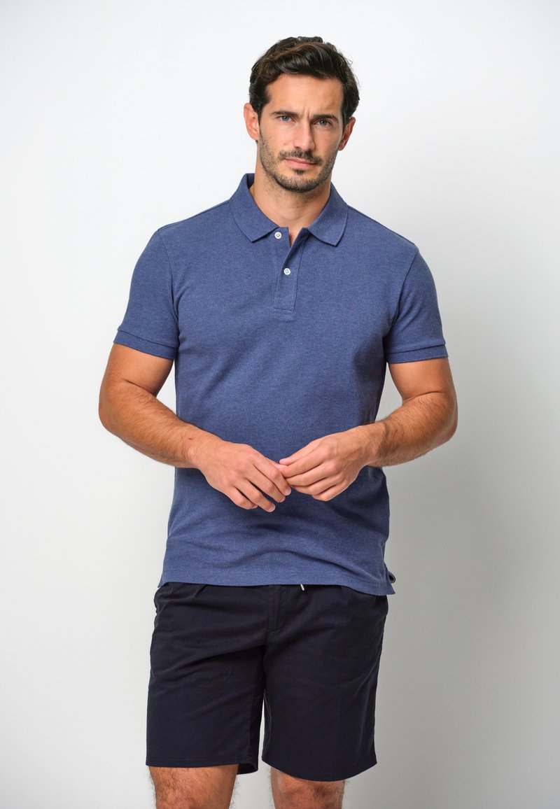 Mörkblå polo t-shirt i ett mjukt, texturerat tyg med klassisk krage och tre knappar. Bärs med mörka shorts.
