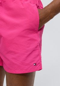 Ροζ μαγιό σορτς από ελαφρύ ύφασμα, με πλαϊνή τσέπη και ένα μικρό λογότυπο σε μπλε, λευκό και κόκκινο στο τελείωμα.