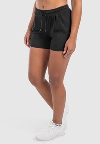 Pantaloni corti neri in cotone con elastico in vita e cordoncino regolabile, caratterizzati da una texture liscia e un design aderente.