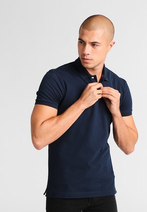 Polo shirt bleu marine en coton avec une texture douce, doté d'un col, de manches courtes et d'une patte de boutonnage à deux boutons.