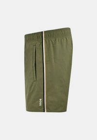 Shorts de bain verts olive en tissu texturé, avec une taille élastique, des poches latérales et une bande contrastante blanche et dorée.