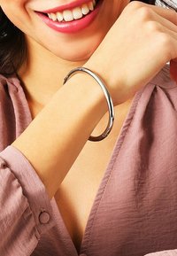 Bracciale rigido in metallo argento su un polso, con un design liscio e arrotondato, finitura lucida e stile minimalista.