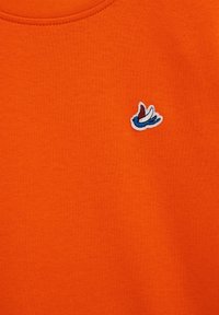 Tissu orange avec un petit oiseau brodé en bleu, blanc et rouge près du centre supérieur.