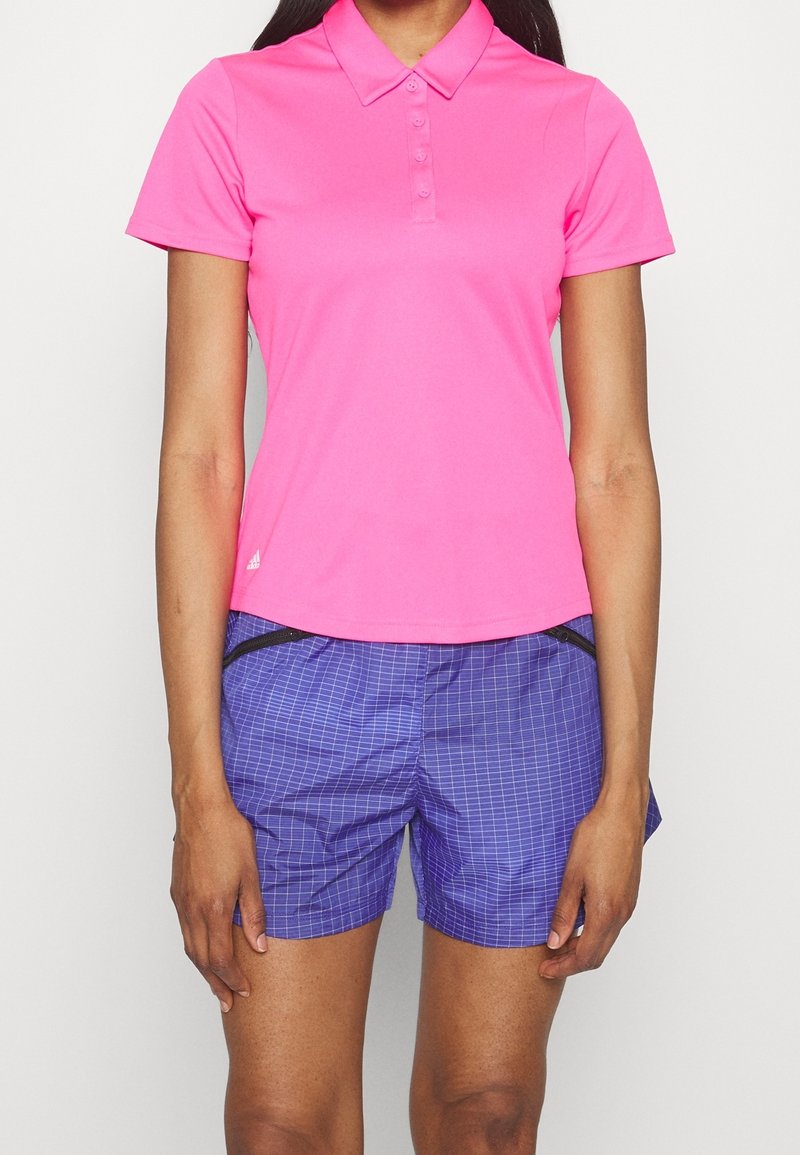 Polo rose avec col et boutons sur le devant, assorti à un short à carreaux bleu comportant une poche latérale et une fermeture éclair noire.