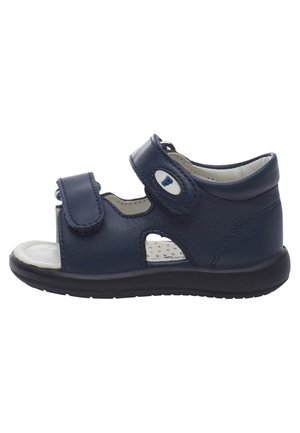 Mørkeblå lædersandal med velcro-rem, perforeret sål og gummibund. Har åbne sider for åndbarhed og komfort.