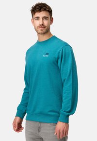Teal sweatshirt lavet af bomuldsblanding; har lange ærmer, ribbede manchetter, rund hals og logodetalje på brystet.