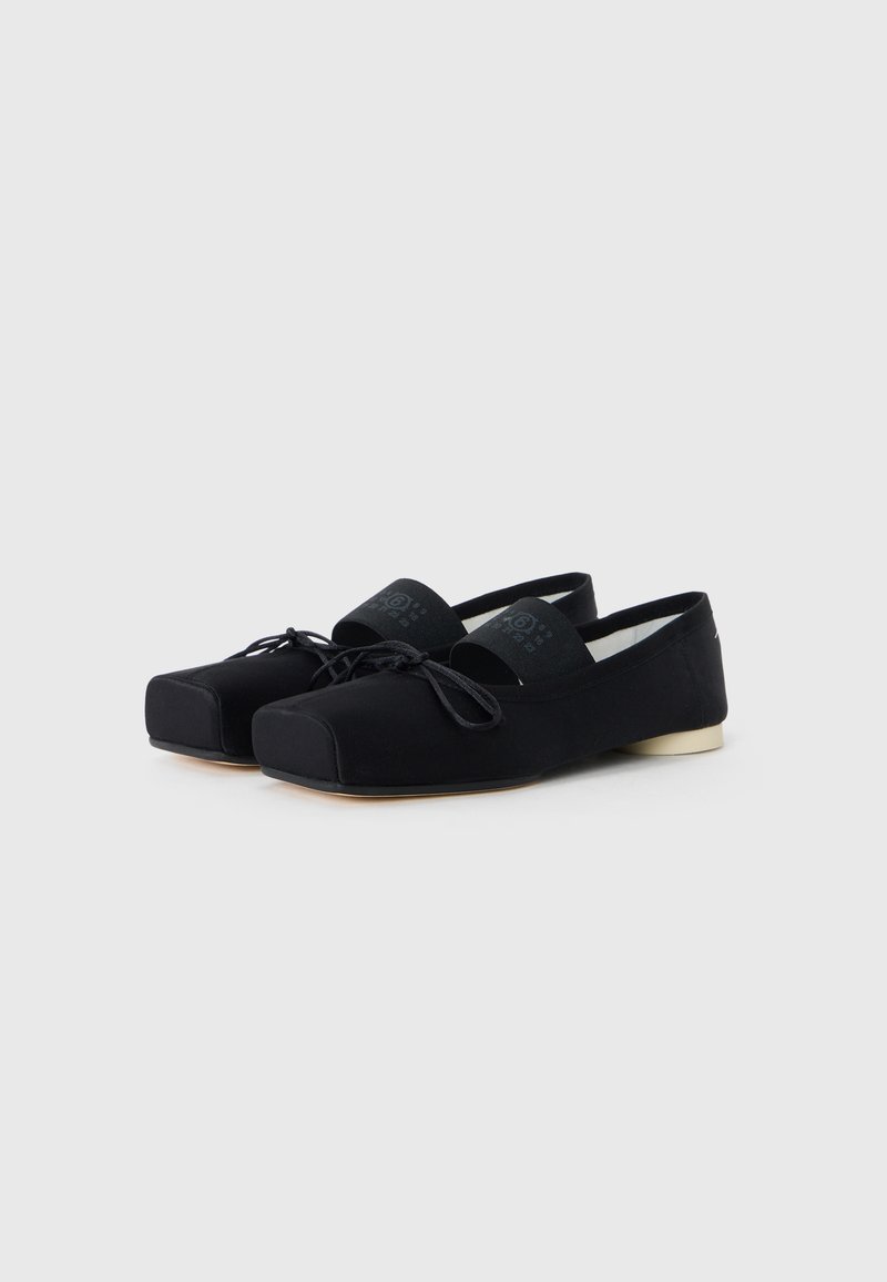 Black flat shoes with a rounded toe, fabric upper, ankle strap, and contrasting white sole. Features a minimal design with laces.