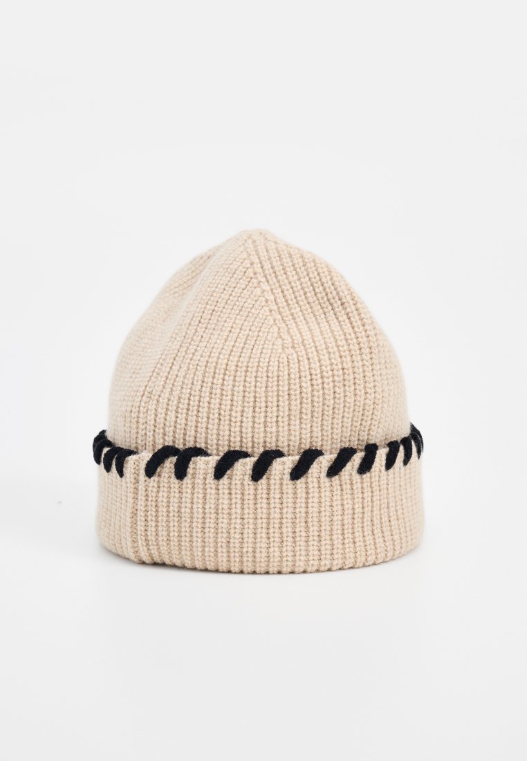 Beige Strickmütze mit strukturierter Oberfläche, ausgestattet mit einem schwarzen dekorativen Stichband am Rand. Oben ist sie rund.