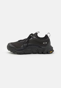 Fekete sportcipő, textúrált hálós felsőrésszel, gumitalppal és lekerekített orral. Fűzőkkel és Vibram díszítéssel a talpon. Oldalnézet.