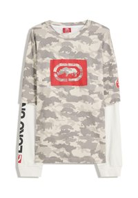 Camicia a maniche lunghe in camuffamento beige e grigio, con un logo grafico rosso sul davanti e scritte nere lungo le maniche bianche. Tessuto strutturato.