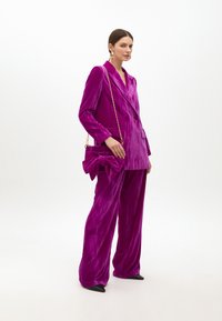 Plush, djup magentaröd kostym med en dubbelknäppt kavaj och byxor med vida ben. I sällskap med en handväska med slife och svarta stilettklackar.