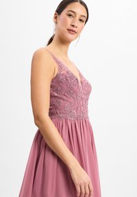 Rosa Kleid mit einem Spitzenoberteil, das komplizierte Stickereien aufweist, zarten Spaghettiträgern und einem fließenden Rock.