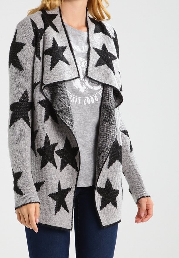 Femme portant un cardigan gris ouvert à l'avant avec de grandes étoiles noires sur un t-shirt graphique gris clair et un jean bleu foncé.