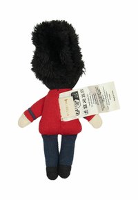Měkká plyšová hračka vojáčka s černou kožešinovou čepicí, červeným uniformou, modrými kalhotami a béžovými rukama; na zadní straně je připevněn štítek s pokyny k péči.