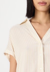 Light yellow striped shirt with a soft fabric, short rolled sleeves, a collar, and white button details.