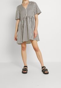 Vestido de manga corta a rayas con escote en V, cintura fruncida y un ajuste fluido. La paleta de colores presenta rayas en crema y oscuro.