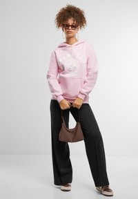 Rožinis džemperis su "LOVERS CLUB" grafika, juodos plačios kelnės, ruda rankinė ir saulės akiniai. Minkšta tekstūra, laisvas kirpimas, paprastas dizainas.