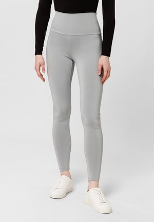 Hoch taillierte graue Leggings aus dehnbarem Stoff, mit einer glatten Textur und einer angepassten Beinform. Kombiniert mit weißen Sneakers.