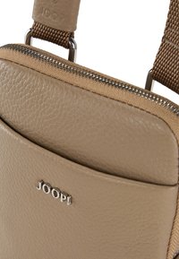 Borsa in pelle beige con finitura texturizzata, con logo argentato e apertura con zip. I dettagli includono una tracolla intrecciata in colore abbinato.