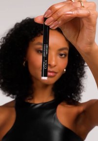 Musta pakkaus hopeisella logolla, jonka kärki on vaaleanpunainen. Malli pitää tuotetta vaaleaa taustaa vasten esitellen sen muotoilua.