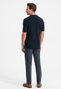 Marinblå kortärmad pikétröja med texturerad yta, kombinerad med slim-fit grå byxor och bruna sko, sedd bakifrån.