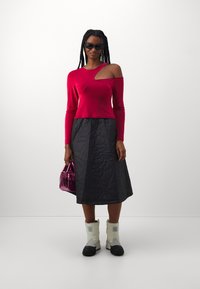 Red long-sleeve top with an asymmetric cut, paired with a quilted black skirt. Accessories include a shiny pink handbag and white boots.